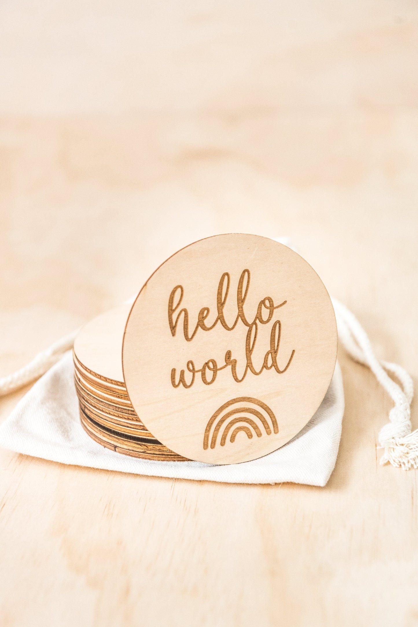 Small round wooden disc with the words 'hello world' and a graphic of a rainbow etched into the wood.